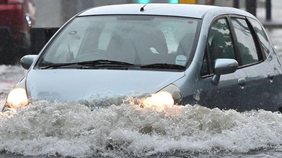 A car is driven through deep water on a flooded road in The Nine Elms district of London