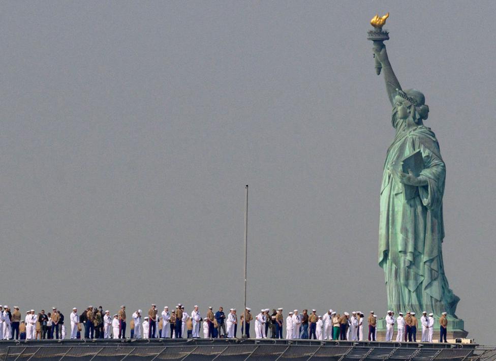 US Sailors and Marines stand on the flight deck of the USS Bataan, a Wasp-class amphibious assault ship, as it passes the Statue of Liberty during Fleet Week in New York Harbour on May 24, 2023.