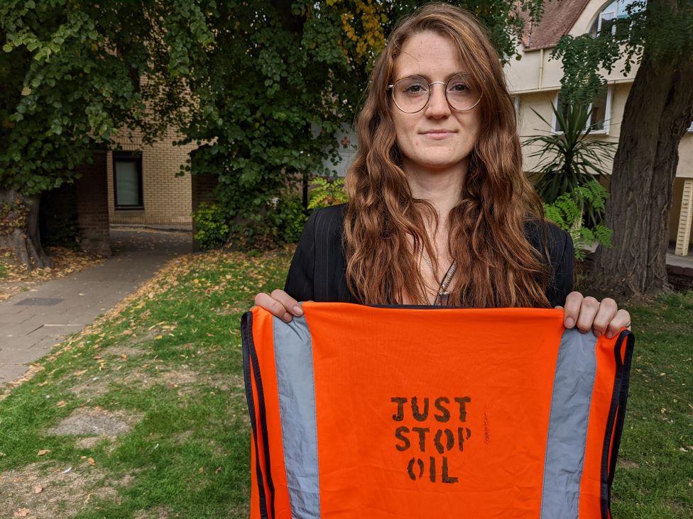 Stephanie Aylett outside Chelmsford Magistrates Court holding up a high viz with Just stop oil written on the back