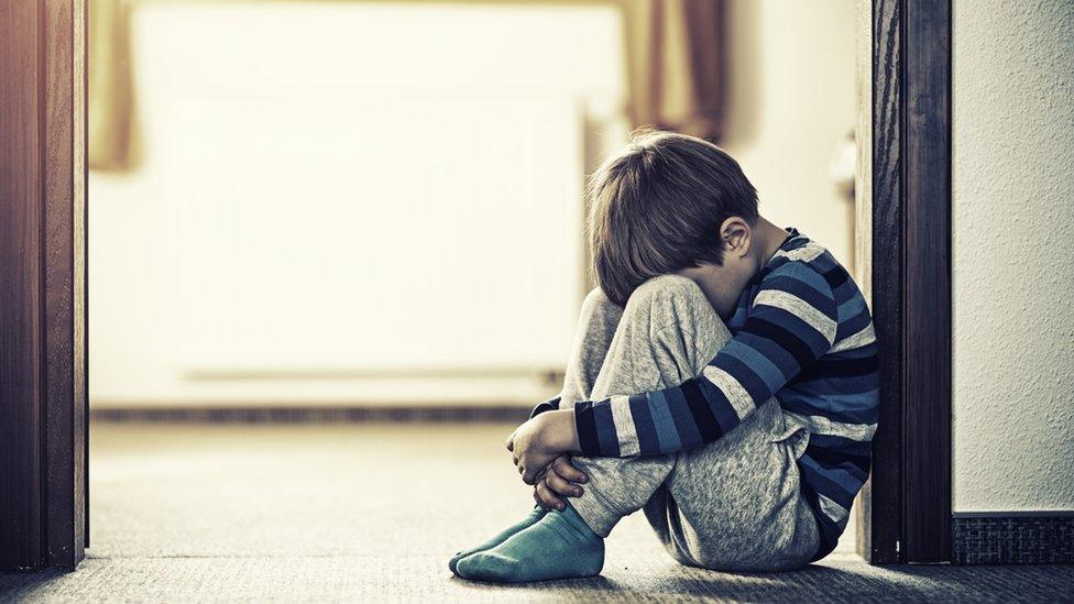 Young boy sitting on the floor with his head between his knees