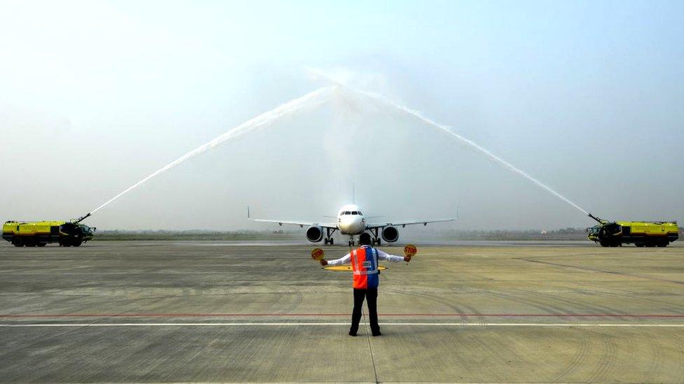 A ground staff directs a Jazeera Airways aircraft to park as it receives a water canon salute upon landing at the newly built Gautam Buddha International Airport following its inauguration in Siddharthanagar on May 16, 2022.