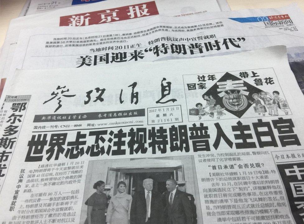 A photograph of several Chinese newspapers, showing a picture of Donald Trump and the Obamas at his inauguration.