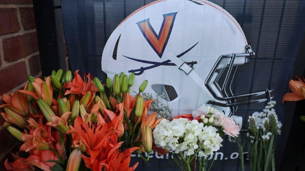 Flowers lay outside a memorial featuring an image of a University of Virginia football helmet