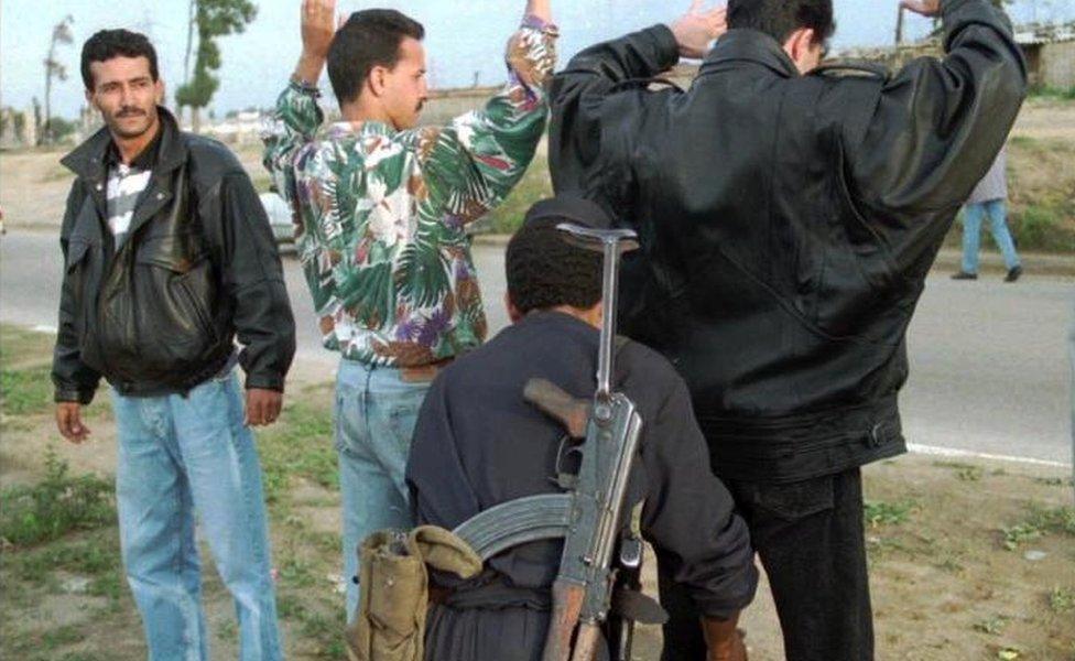 An Algerian police officer searches passengers from a bus stopped at a check point during routine control in the suburb of Algiers, November 1995