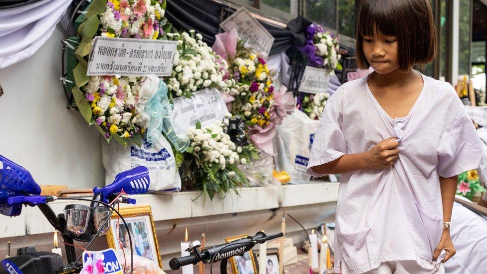 A girl stands near a bike which is kept as an offering to the children victims around the temple outside Wat Rat Samakee during their funeral, in the town of Uthai Sawan in Thailand