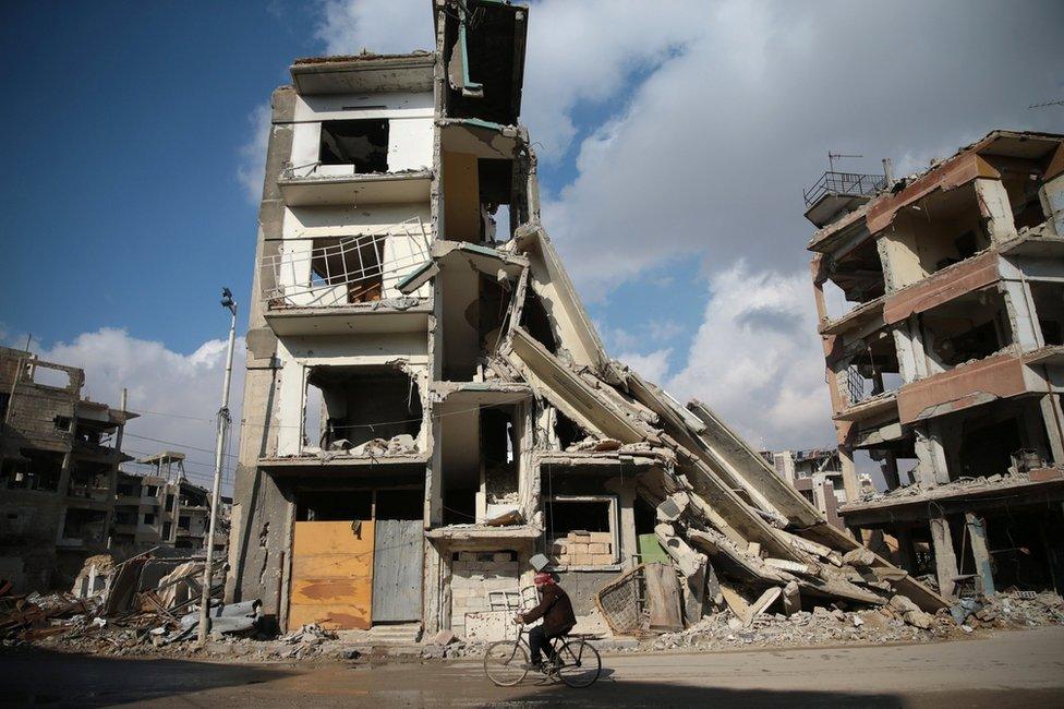 A man cycles past a damaged building in the rebel-held Damascus suburb of Douma (30 December 2016)