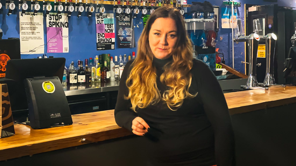 Carly Heath leaning on a bar with alcohol in the background