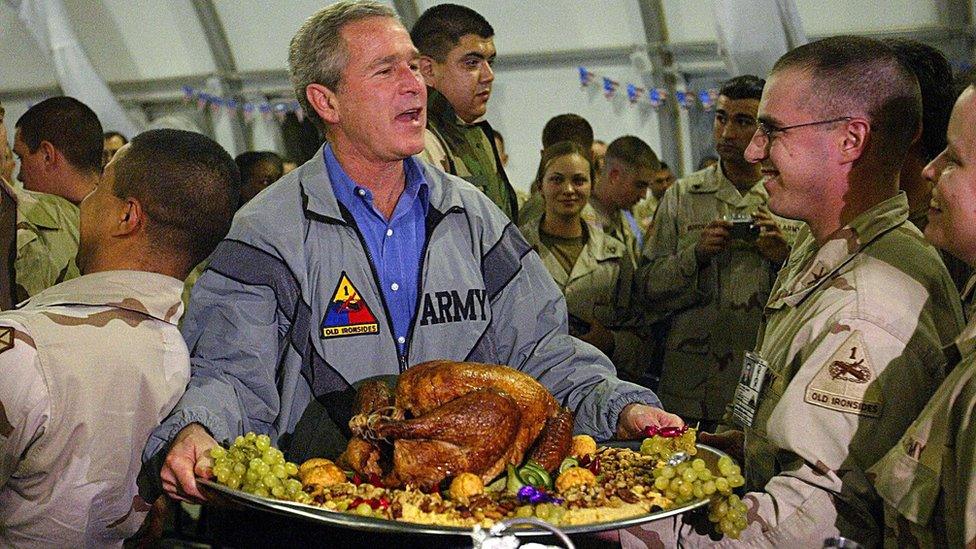 US President George W Bush carries a platter of turkey and trimmings as he visits US troops for Thanksgiving in Baghdad on 27 November 2003 in a top-secret visit