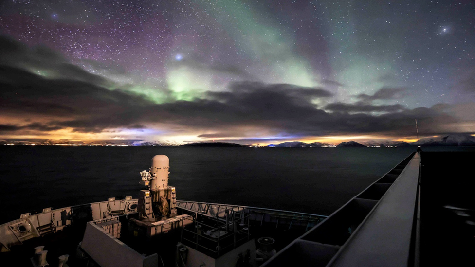 HMS Albion's bow against the backdrop of the Norwegian Fjords under the backlight of the Aurora Borealis