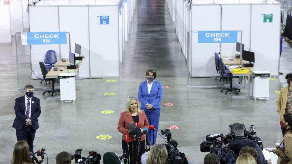 Deputy First Minister Michelle O'Neill addressing a crowd at the SSE Arena, with First Minister Arlene Foster behind her and Health Minister Robin Swann also in view