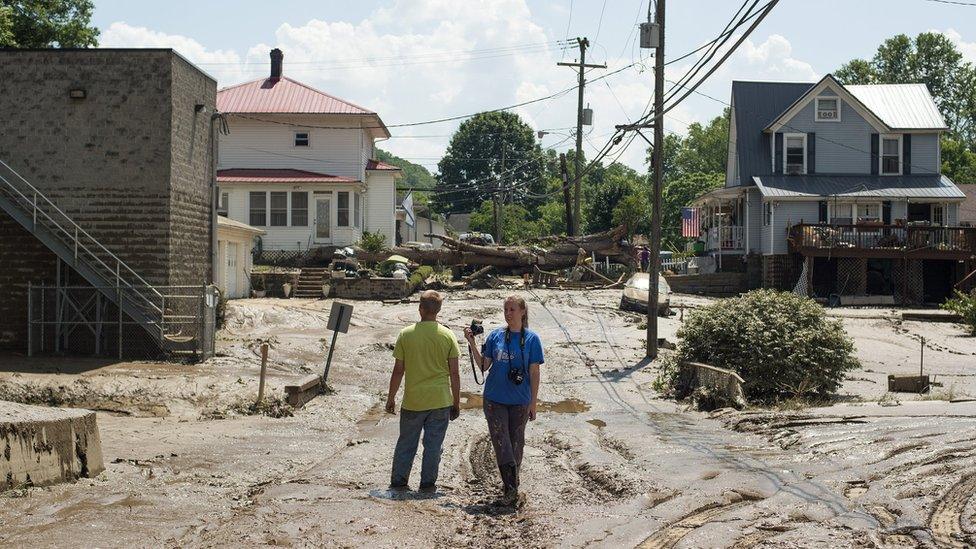 People stand in mud covered street after flooding of Elk River on June 25, 2016 in Clendenin, West Virginia