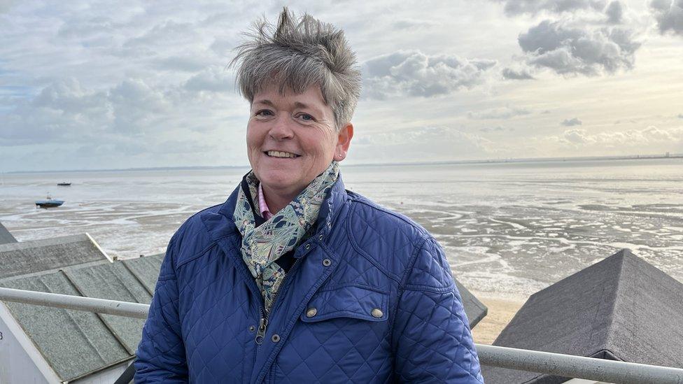 A woman wearing a blue coat standing at Thorpe Bay in Essex smiling at the camera