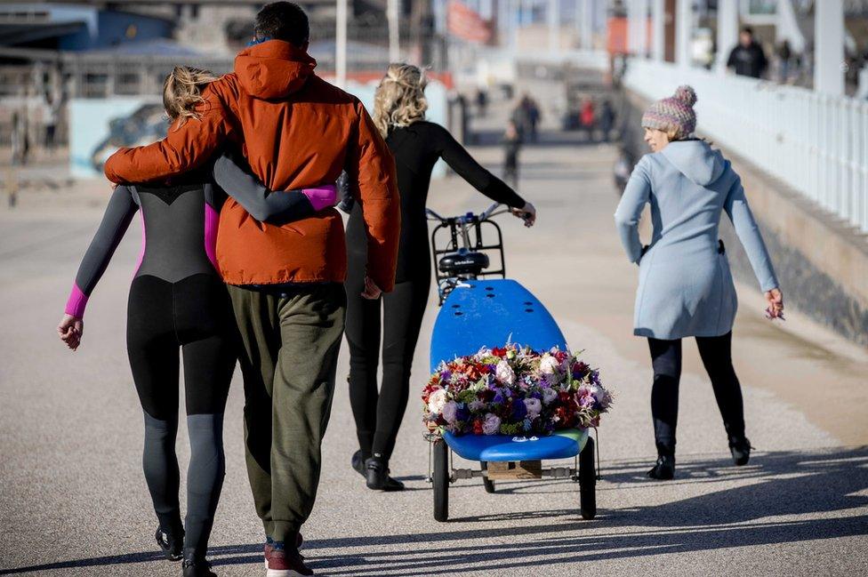 Surfers arrive with a wreath on a surfboard at the surf club "The Shore" to commemorate the deceased surfers