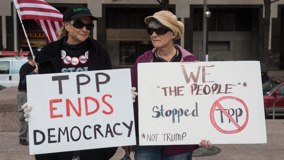 People hold signs as they demonstrate against the Trans-Pacific Partnership (TPP) trade agreement