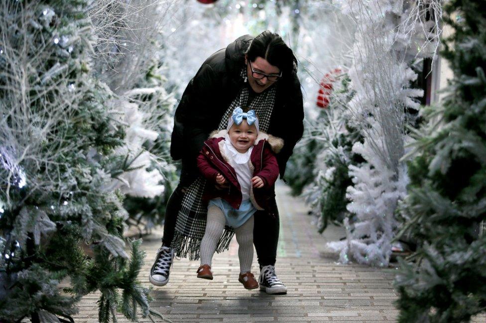 A mother plays with her baby at a display of Christmas trees in Belfast