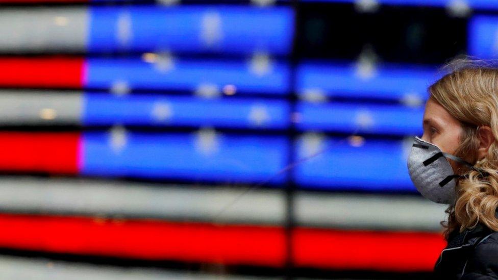 A person in a surgical mask walks by a reflection of the flag of the United States as the coronavirus outbreak continued in Manhattan, New York City