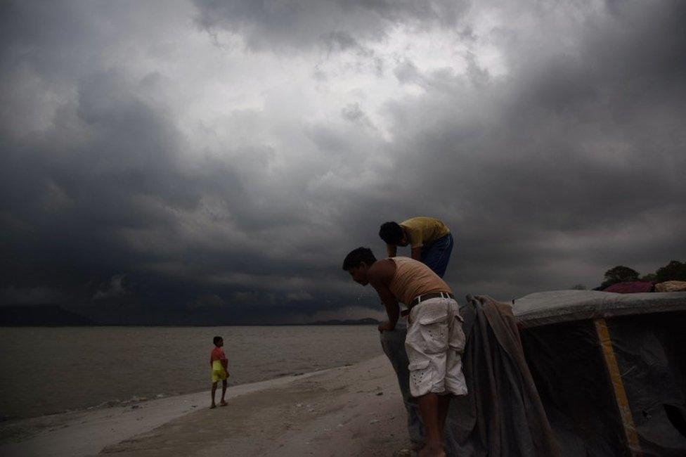 Indian boatmen cover their boat on the banks of the river Bramaputra as rain clouds loom over Guwahati on May 13, 2016.