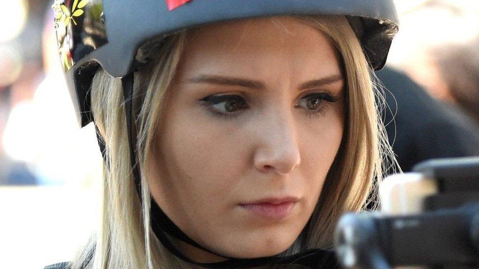 Lauren Southern, wearing a helmet, filming a crowd on a smart phone.