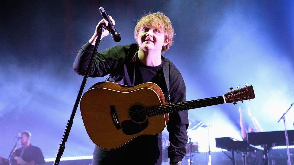 Lewis Capaldi, holding microphone and a guitar