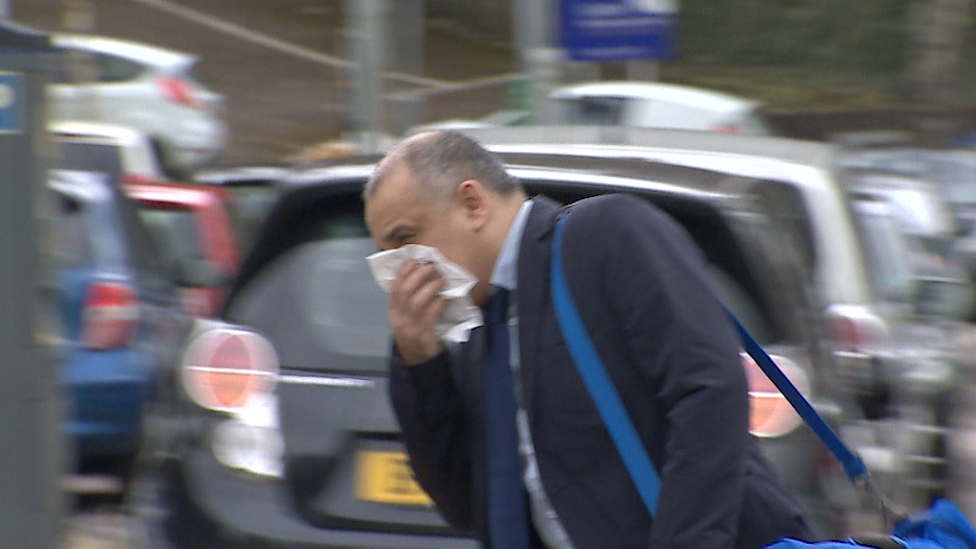 Rajesh Lama arriving at Newport Crown Court - he is trying to hide his face with a tissue. He is wearing a suit and had a blue holdall bag over his shoulder