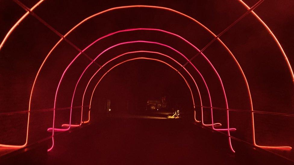 Arched rows of lights in pink and orange hues sit a slightly blurry darkness because of a dry ice smoky effect