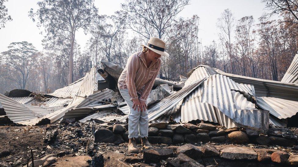 Ms Plesman stands on top of the remains of her home following a wildfire