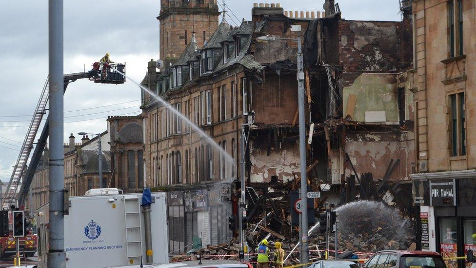 A fireman on top of a platform sprays water on a building adjacent to the collapsed building