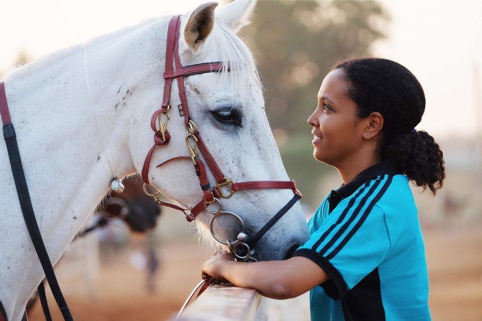 A woman stands close to a horse, holding it by its reins.