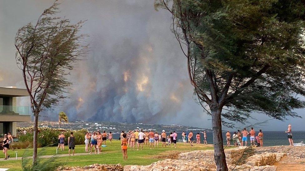 People looking at smoke billowing from a wildfire in Rhodes