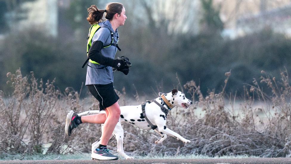 A woman and her dog run along the bank of the River Cam in Cambridge at sunrise on 17 January 2023