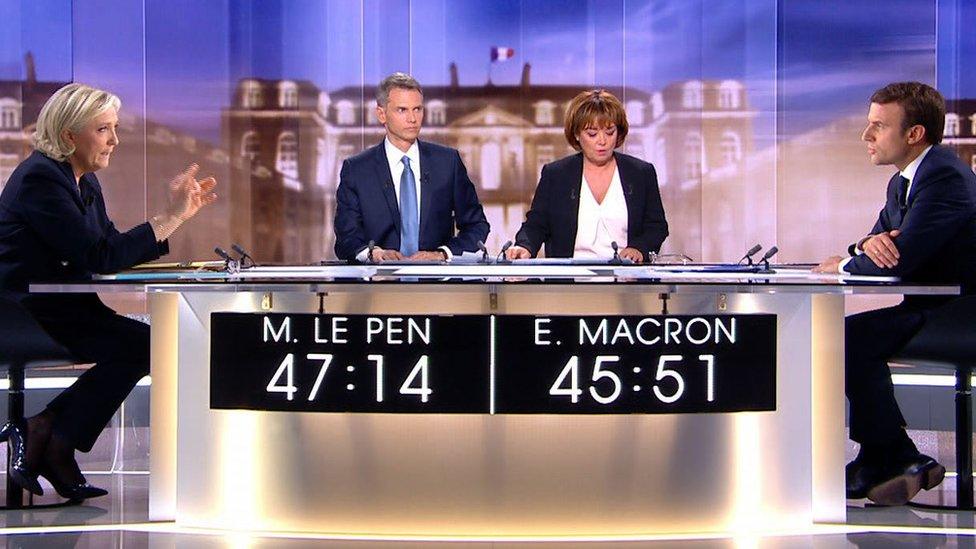 A still from the debate shows both candidates facing each other over a table with the moderators