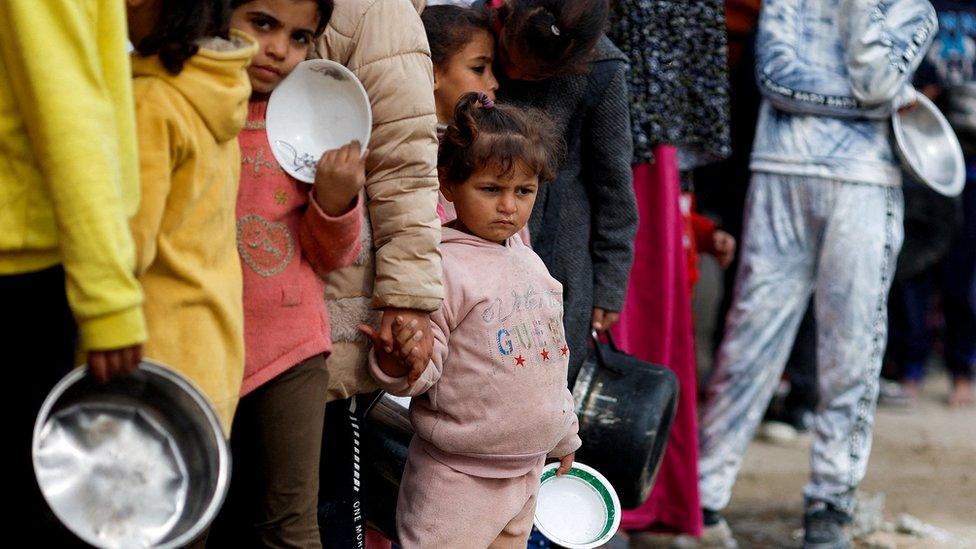 Palestinian children stand in a line as they wait to receive food amid shortages of food supplies,