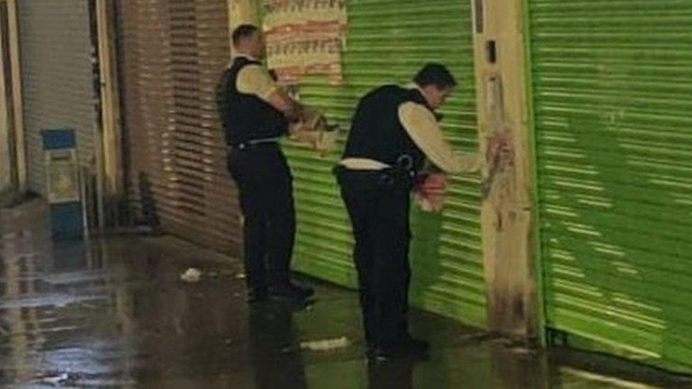 Two officers removing hostage posters from business shutters in Edgware
