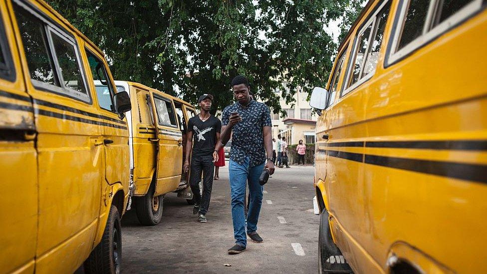 Pokeman Go mania in Nigeria with two young men walking between buses whilst playing the game on their mobile phones