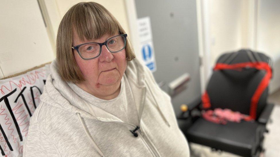 Carol Aldridge standing next to her front door and wheelchair.