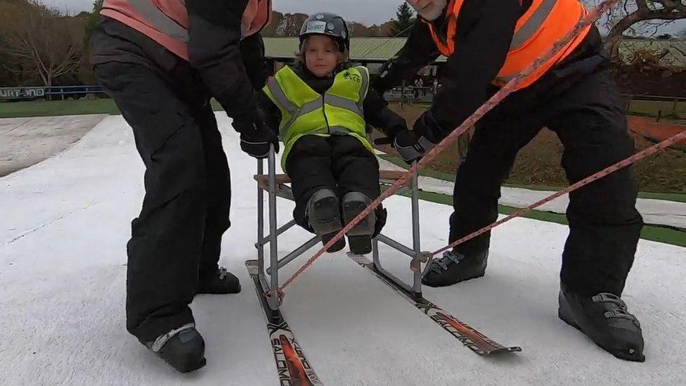 A little boy in a specially constructed chair to help him reach the top of the ski slope