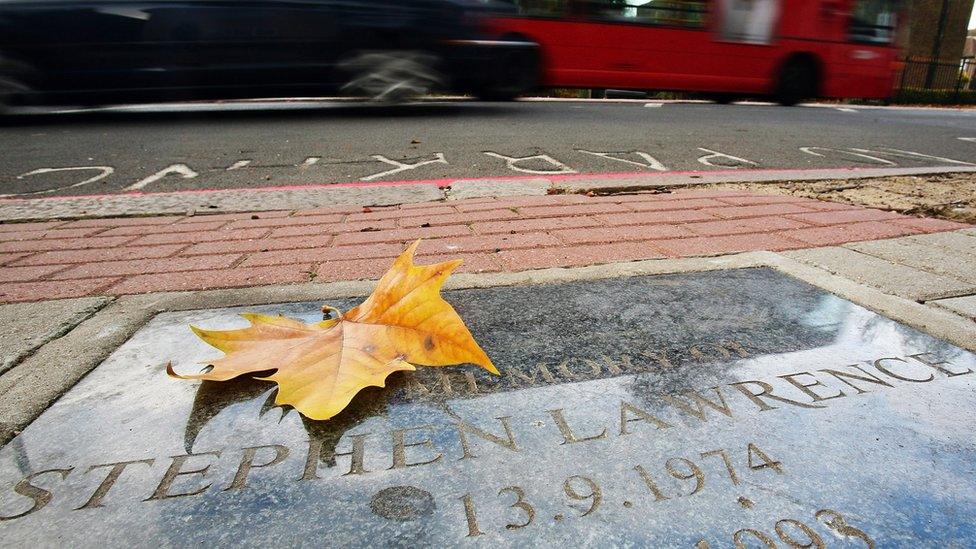 A leaf lying on the memorial plaque for Stephen Lawrence, as a car and bus drive past