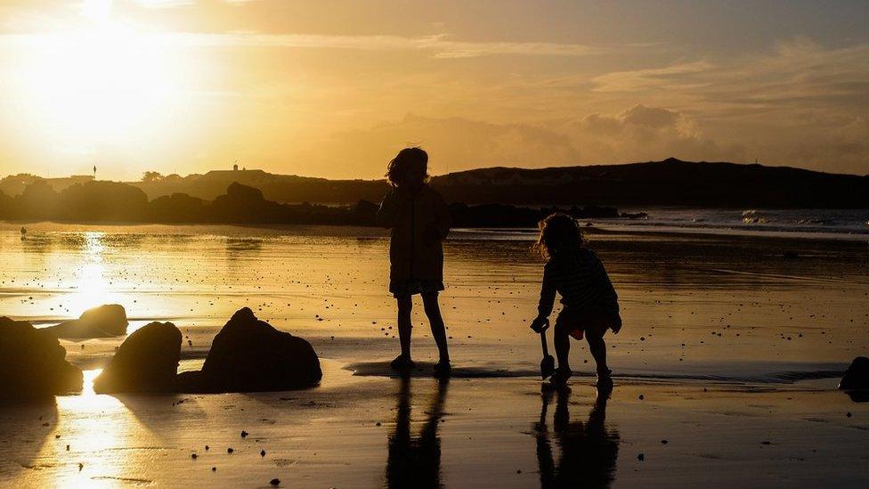 Two children playing on a beach at sunset