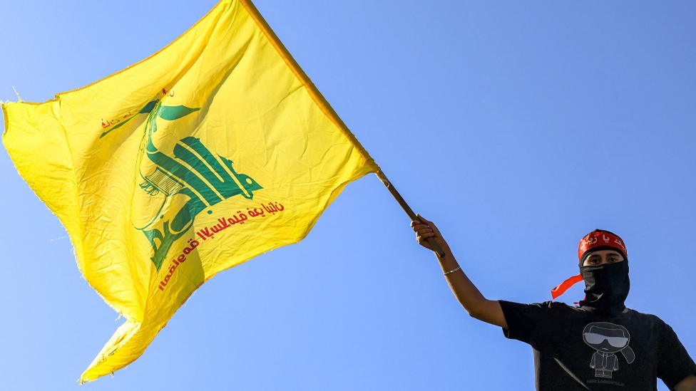 A masked demonstrator waves a flag of the Lebanese Shiite movement Hezbollah during a demonstration