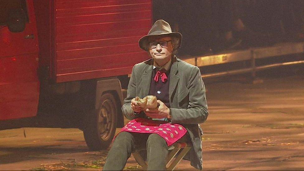 Actor sitting down eating a sandwich as milk floats drive by during opening ceremony of Gotthard rail tunnel - 1 June 2016