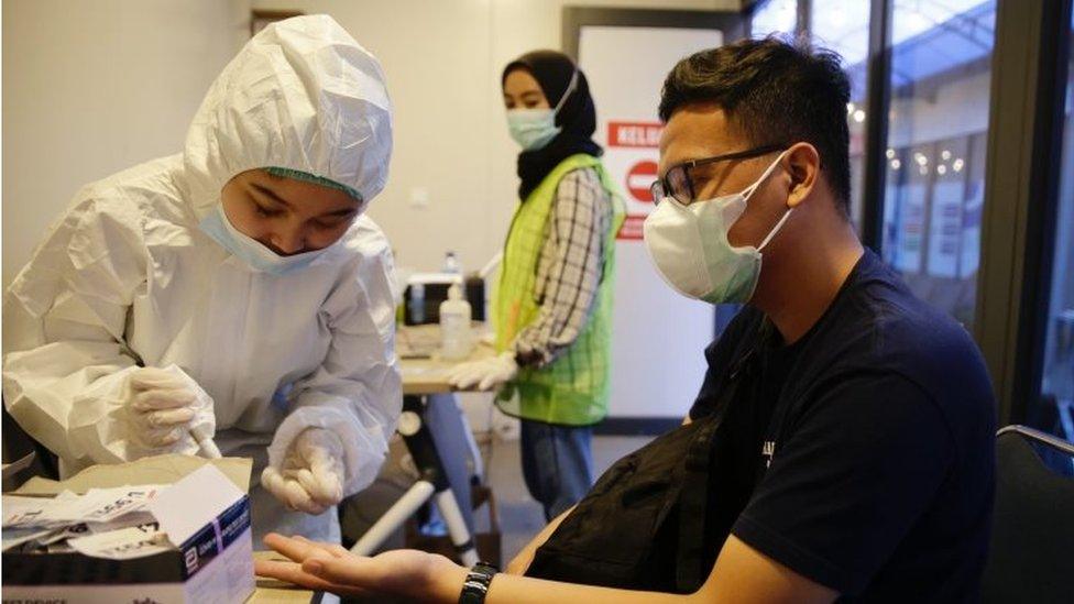 A healthcare worker in hazmat suit collects samples from a plane passenger at Soekarno-Hatta International airport in Banten, Indonesia, 24 December 2020.