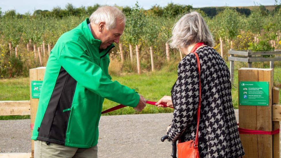 A red ribbon being cut in front of the new community woodland