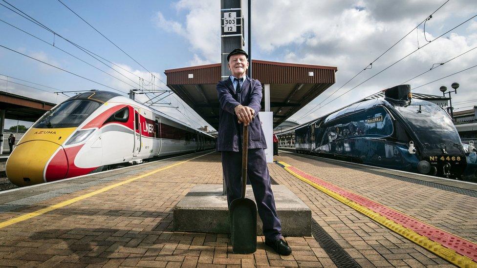 Steam train worker standing on a platform holding a shovel, with Mallard on his right