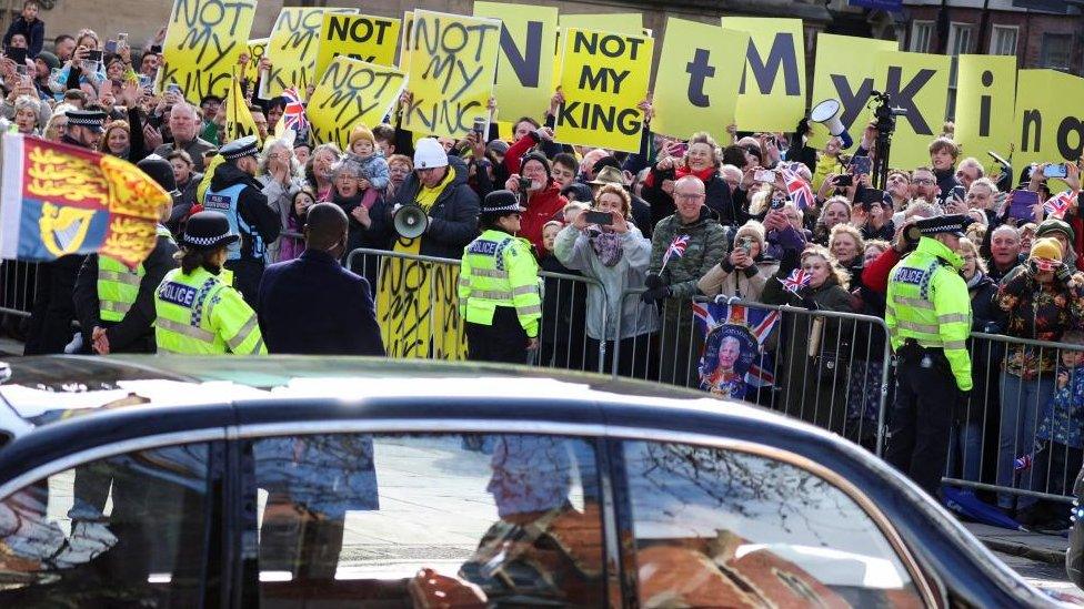 A car carrying King Charles passes anti-monarchy protesters