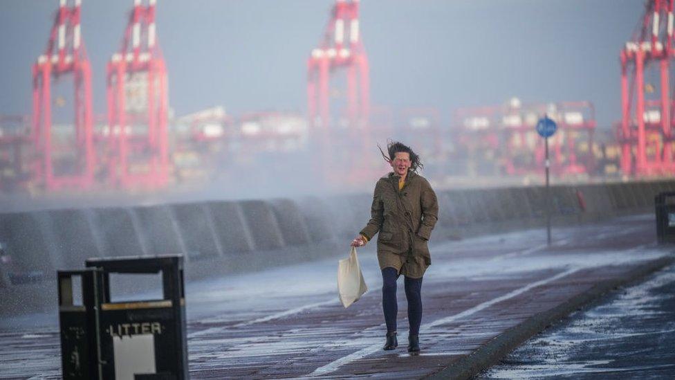 woman battles the wind as she walks along the coast