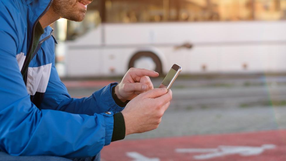 Man plays with his phone at a bus stop