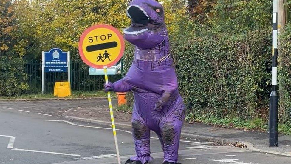 Eight foot purple dinosaur on patrol helping children cross a road in Edith Weston, Rutland