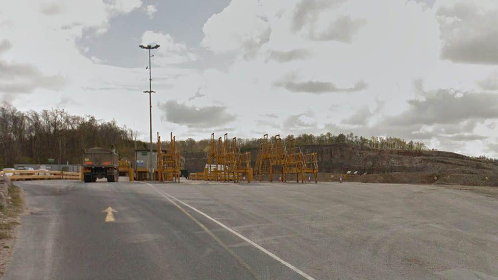 General view of the road leading to Leapers Wood quarry, with a lorry to the left, yellow scaffolding in the middle and the quarry rock in the background