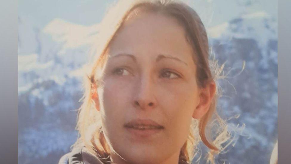 Joanna Hills, looking slightly off to the left, she has long hair, tied back, with tendrils falling around her face. She has fair hair.
