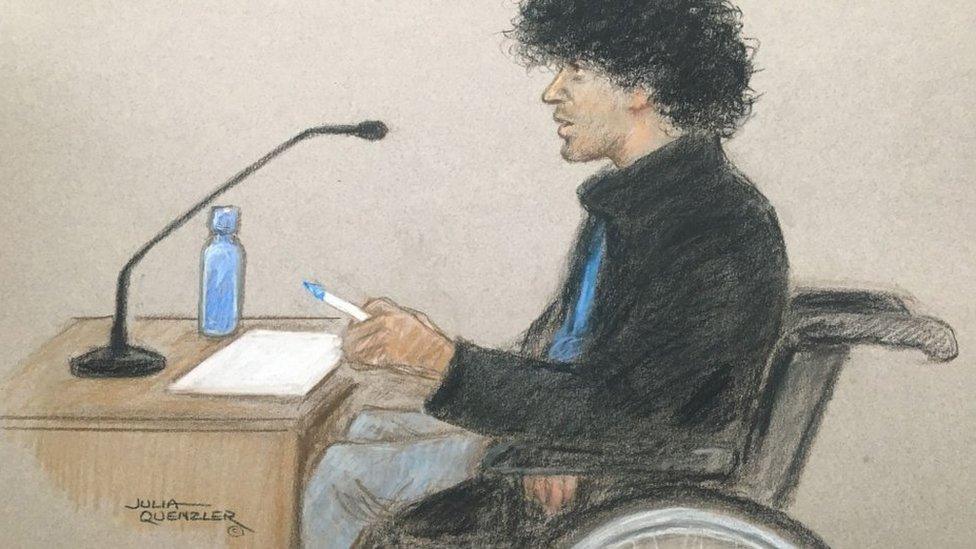 Mr De Zoysa appearing in court in a wheelchair on Tuesday, wearing a black jacket and blue top, using a whiteboard and pen.